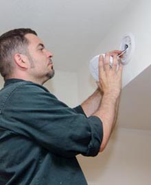 photo : installation d'un détecteur de fumées sur la partie haute d'un mur (par un homme)