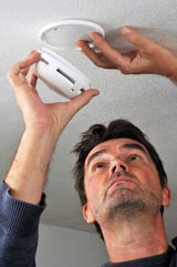 photo : installation d'un détecteur de fumées au plafond (par un homme)